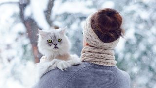 Cat being held by woman, looking over her shoulder in the snow